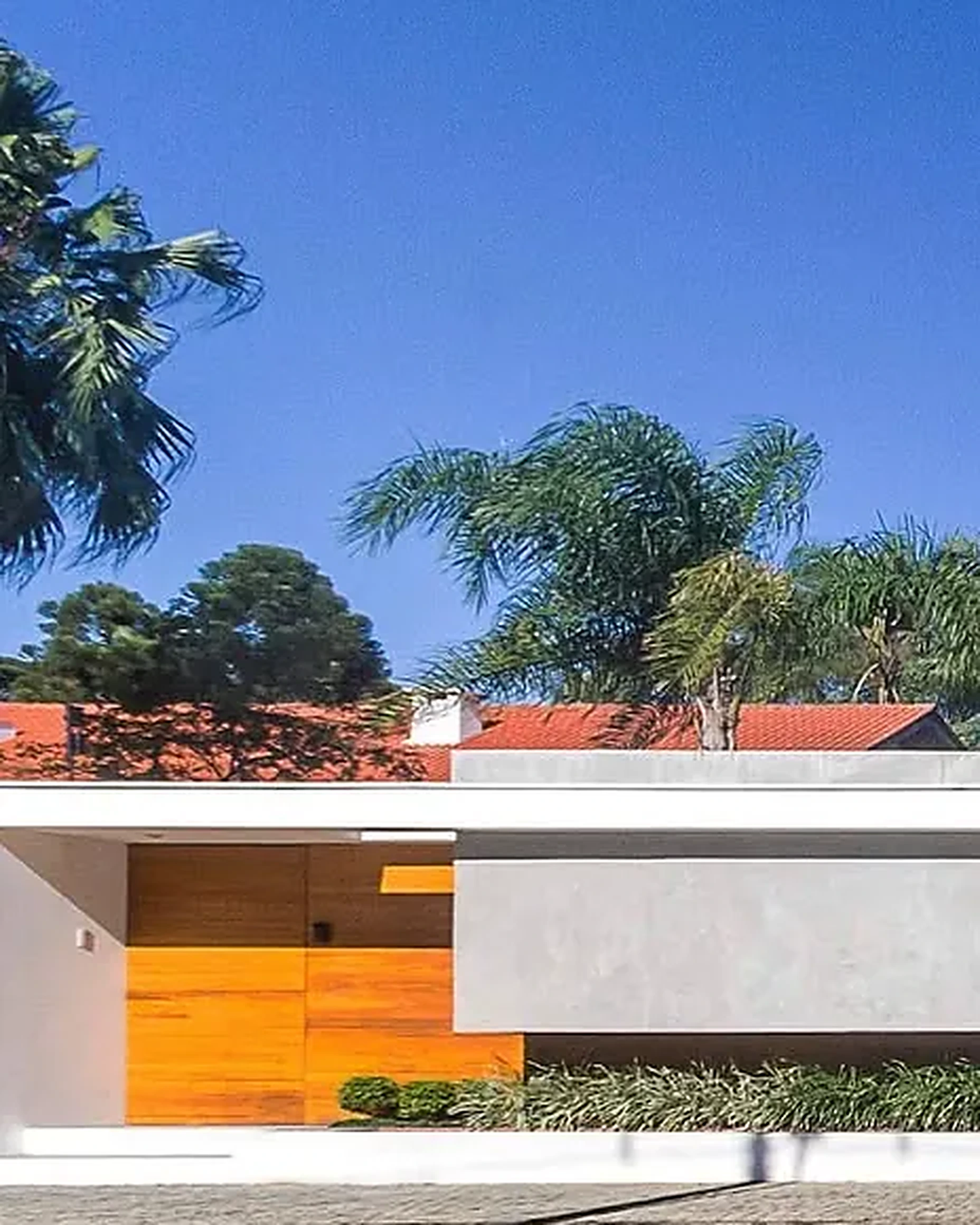 Fachada de residência térrea com volume branco e porta em madeira